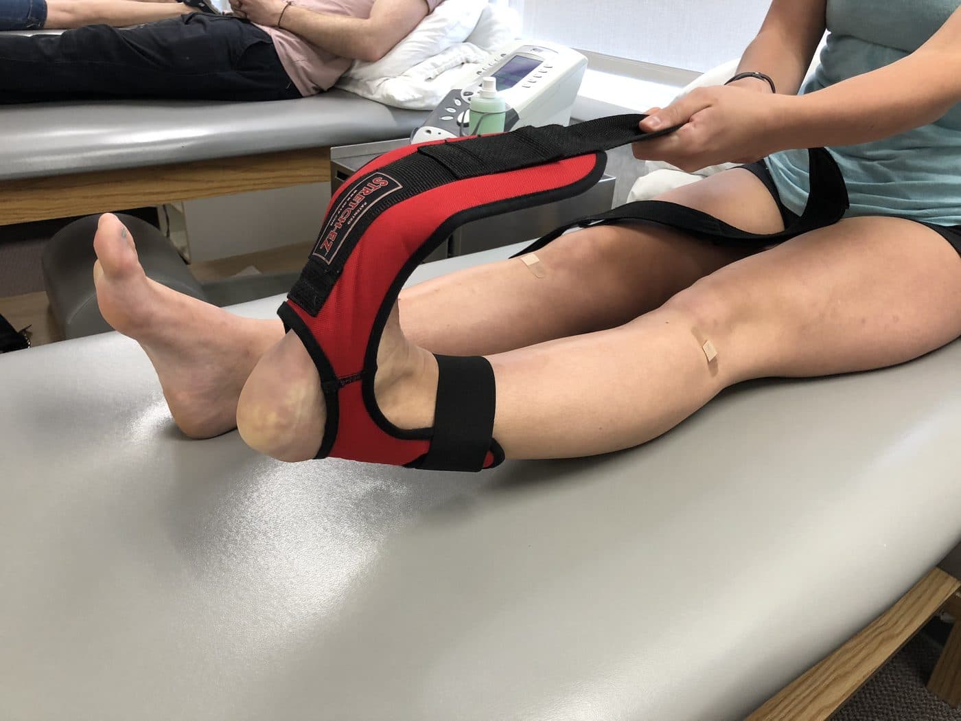 Patient using a leg stretching strap on a treatment table